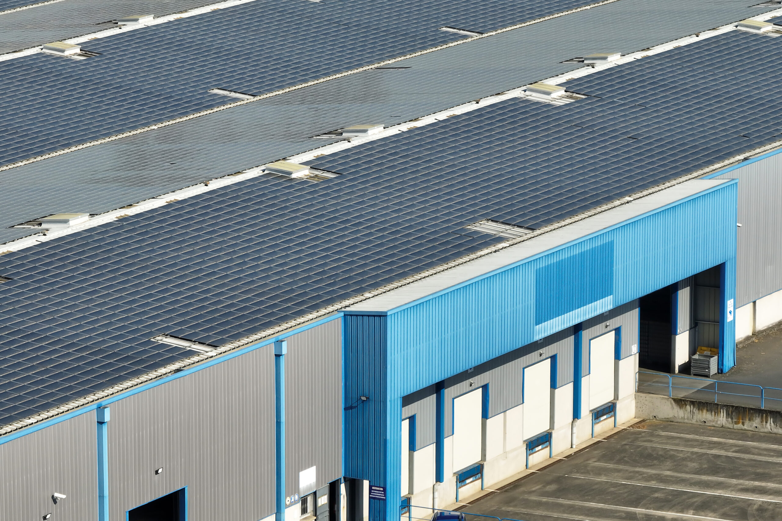 Aerial view of blue photovoltaic solar panels mounted on industrial building roof for producing green ecological electricity